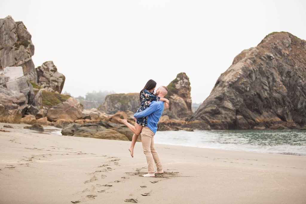 guy holding girl in the air on rocky beach