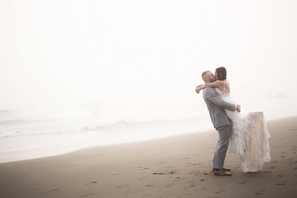 newlyweds kissing on the foggy beach
