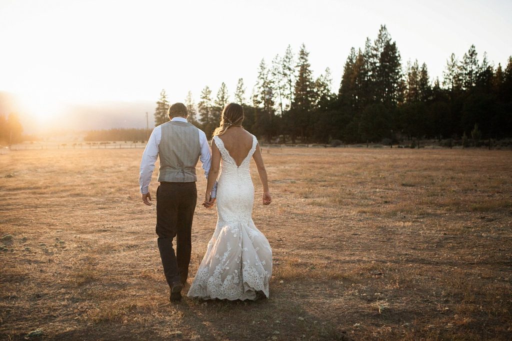 newlyweds walking in field at sunset