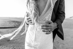 Groom holding bride's waist on a windy beach