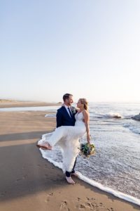 groom holding bride near the ocean waves