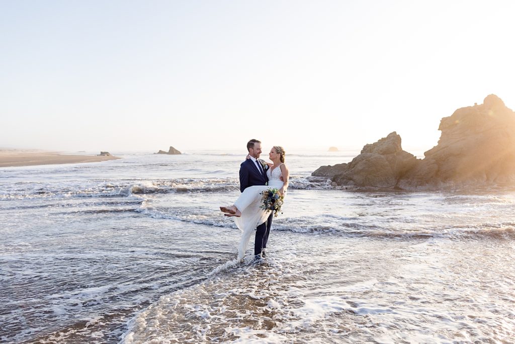 groom holding bride while the ocean waves surround them