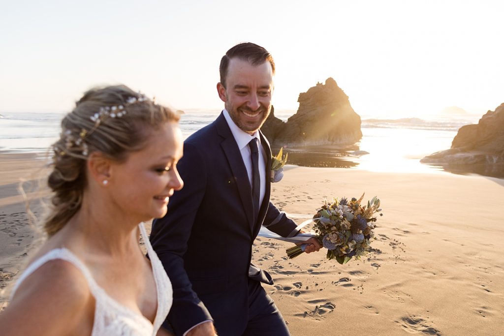 smiling newlyweds walking on the beach at sunset