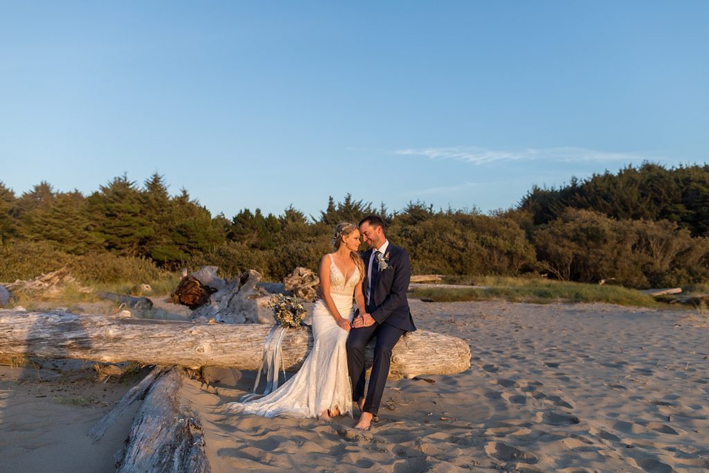 bride and groom sitting on driftwood