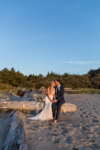 newlyweds sitting on driftwood and kissing